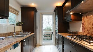 A modern kitchen with dark cabinetry, a stainless steel sink, a built-in oven, and a gas stove. - The Chelsea Apartment (London)