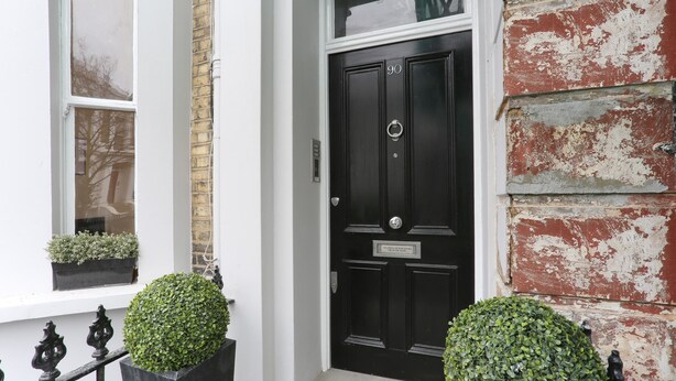 A black door with a sign, a white window with a plant, and a red brick wall. - The Chelsea Apartment (London)