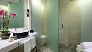 A modern bathroom with a large mirror, a round sink, a glass shower enclosure, and a potted orchid.