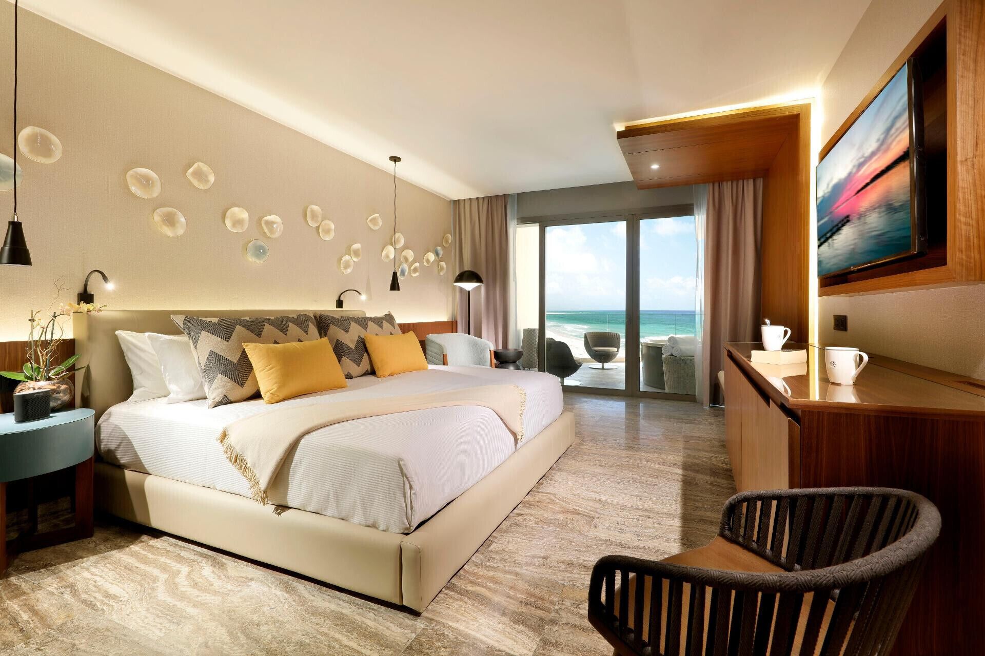 A modern hotel room with a large bed, a desk, and a view of the ocean.