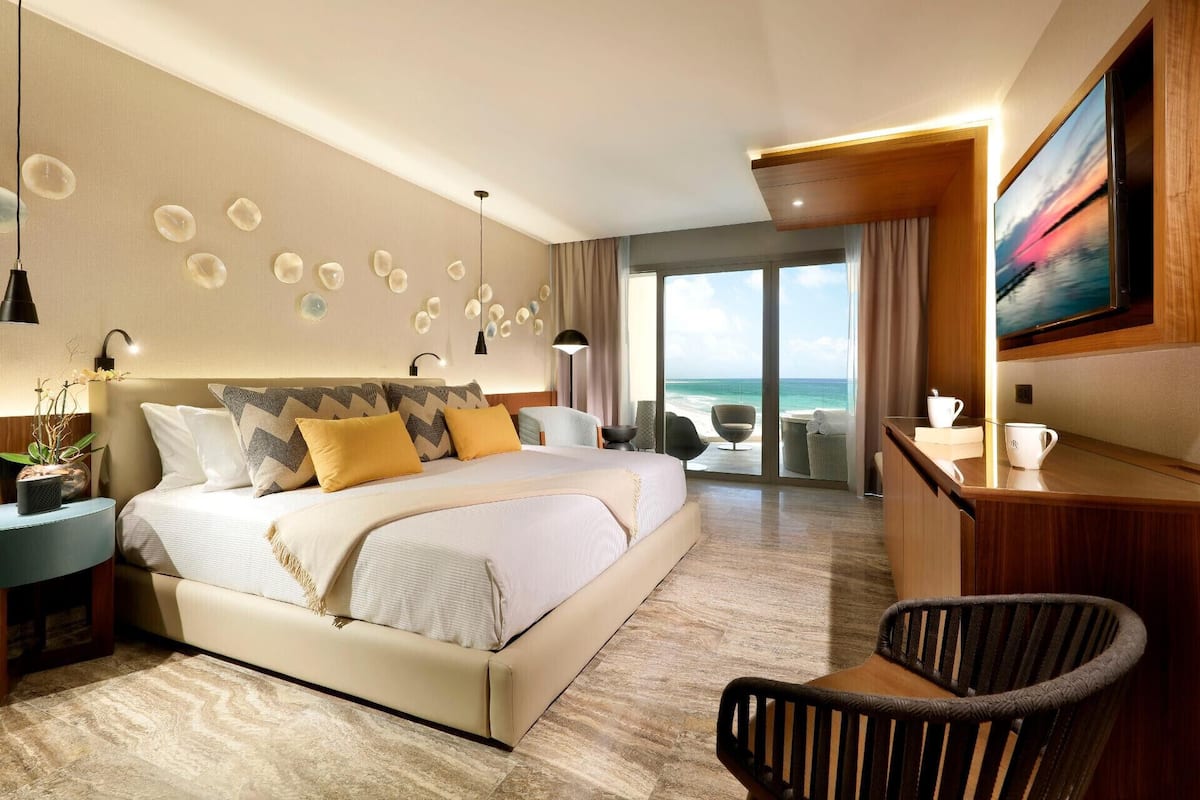 A modern hotel room with a large bed, a desk, a chair, and a view of the ocean.