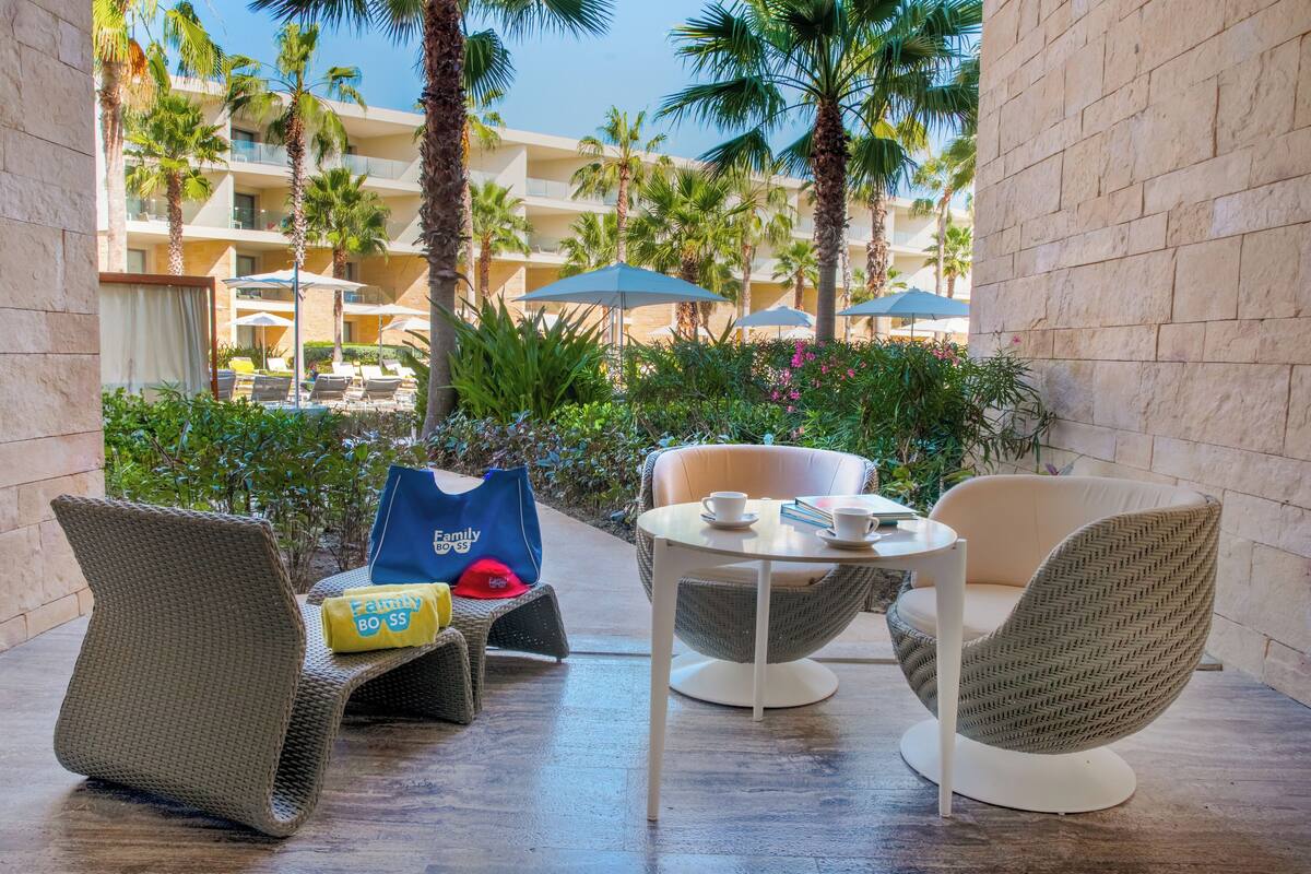 A hotel patio with wicker furniture, a table with cups, and a view of the hotel building and palm trees.