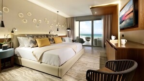 A modern hotel room with a large bed, a seating area with a view of the ocean, and a wooden desk with a television. - Family Selection at Grand Palladium Select Costa Mujeres - All Inclusive (Costa Mujeres)