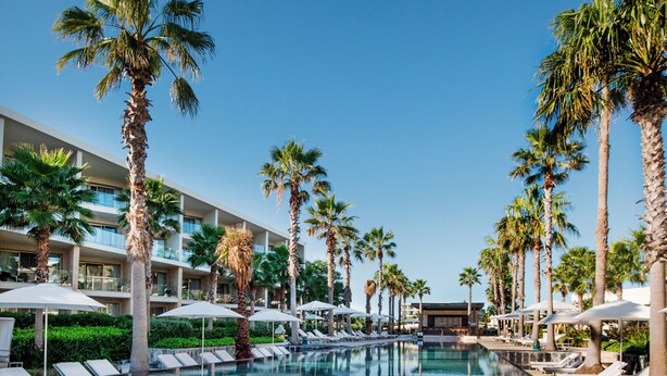 A clear pool surrounded by palm trees and lounge chairs, with a modern building in the background. - Family Selection at Grand Palladium Select Costa Mujeres - All Inclusive (Costa Mujeres)