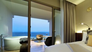 A hotel room with a large bed, a glass door leading to a balcony with a view of the sea, a bathtub, and a table with a glass of wine. - Family Selection at Grand Palladium Select Costa Mujeres - All Inclusive (Costa Mujeres)