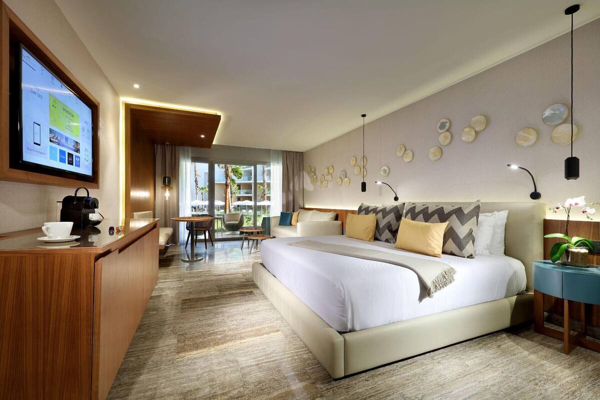 A hotel room with a bed, a desk, a TV, and a view of the outside.