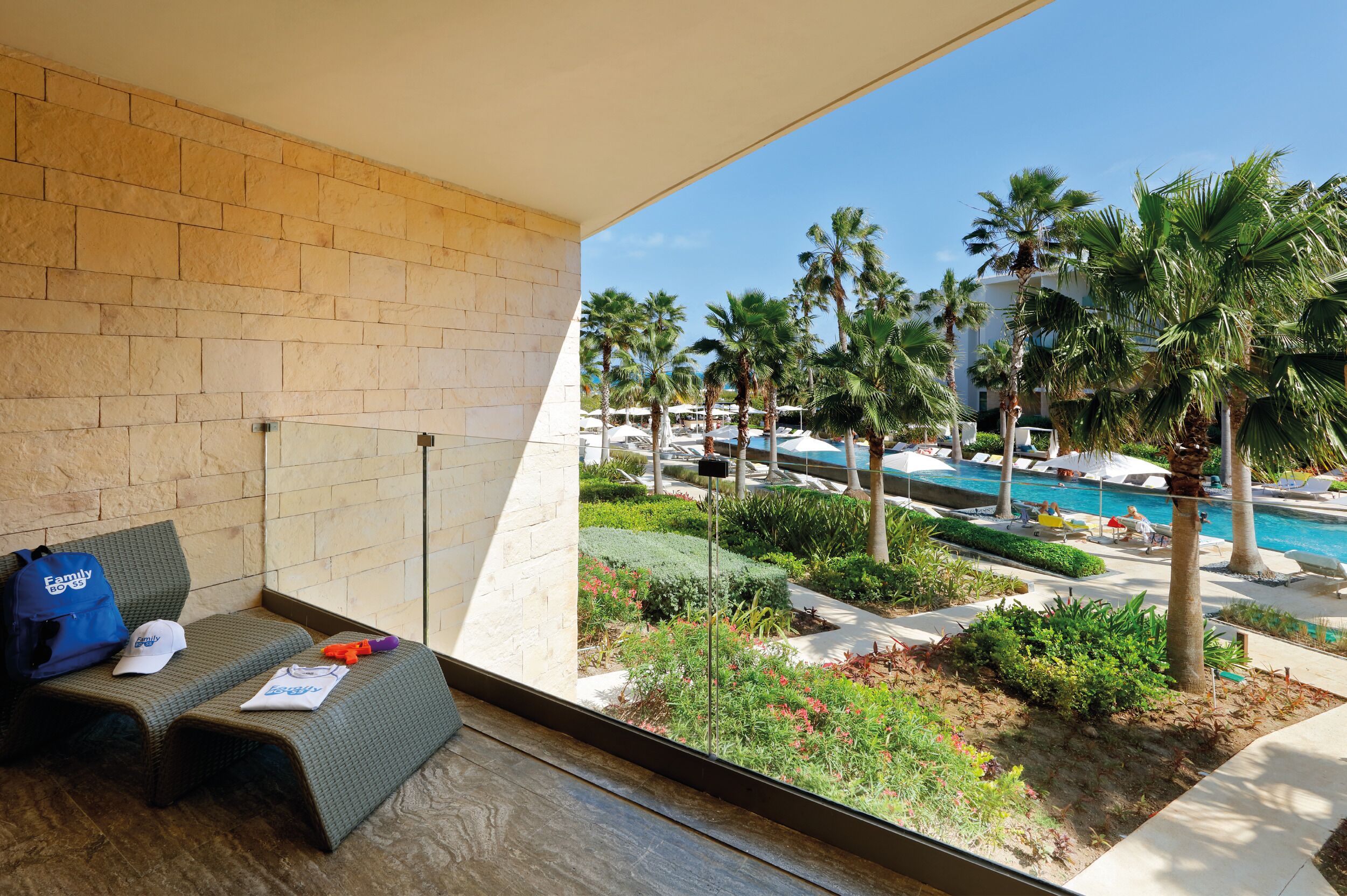 A balcony with a view of a pool area, palm trees, and a brick wall.
