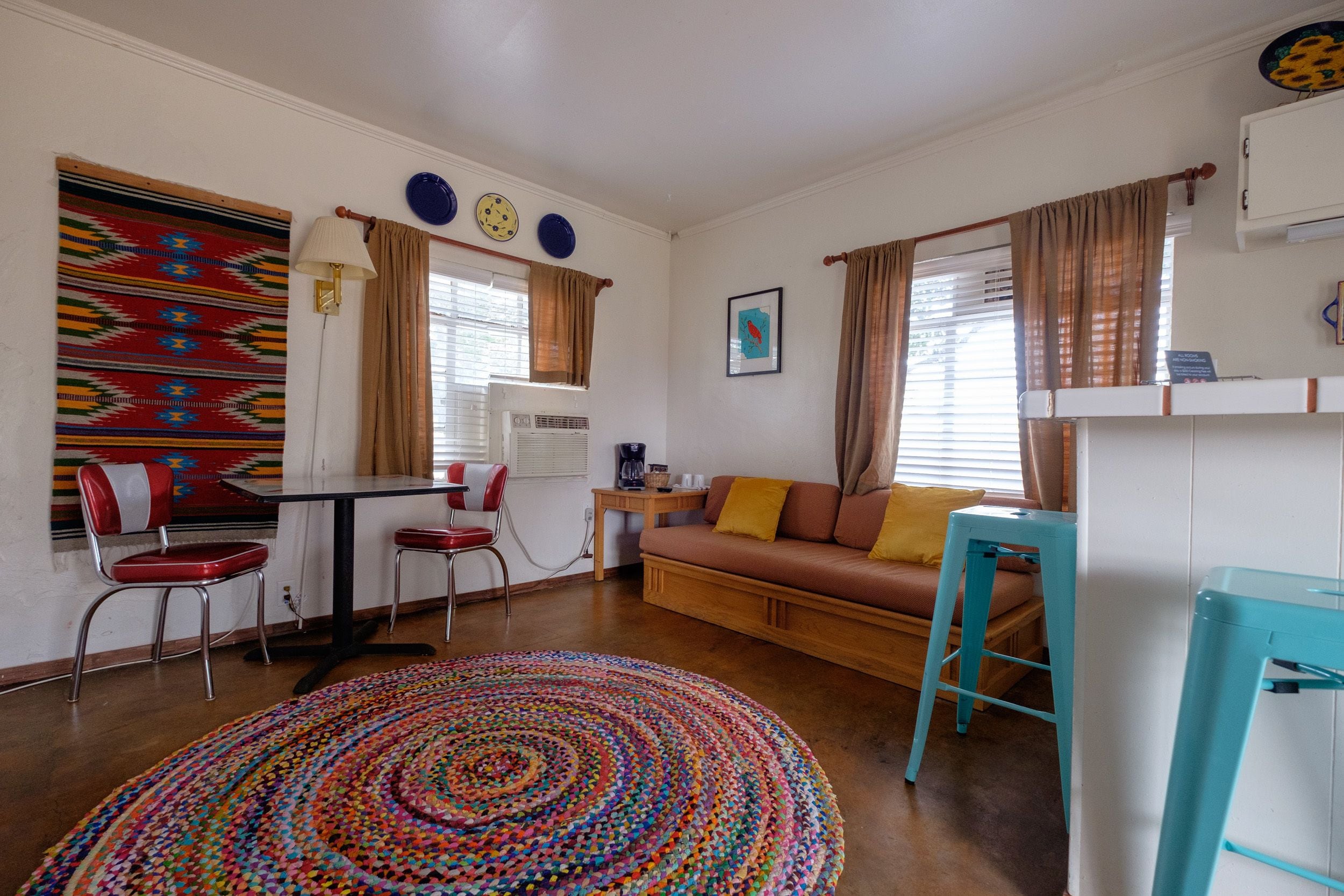 A compact living space with a dining area, a sofa, a colorful rug, and a kitchenette.