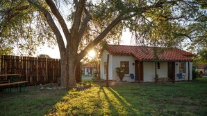 Una casa con techo de tejas, cerca de madera y un árbol proyectando sombras sobre el césped.
