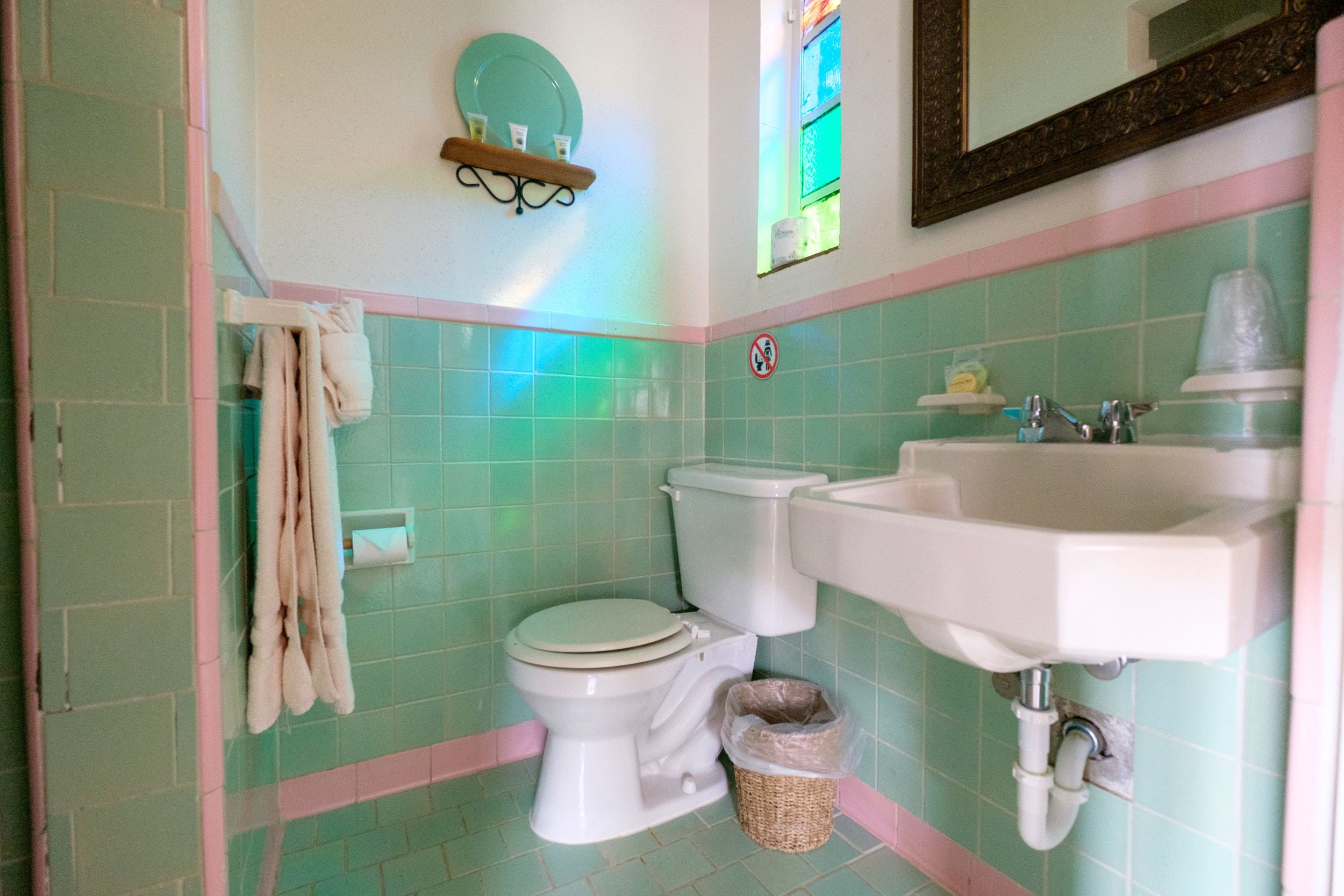 Une salle de bain avec des carreaux verts, un lavabo blanc et des toilettes.
