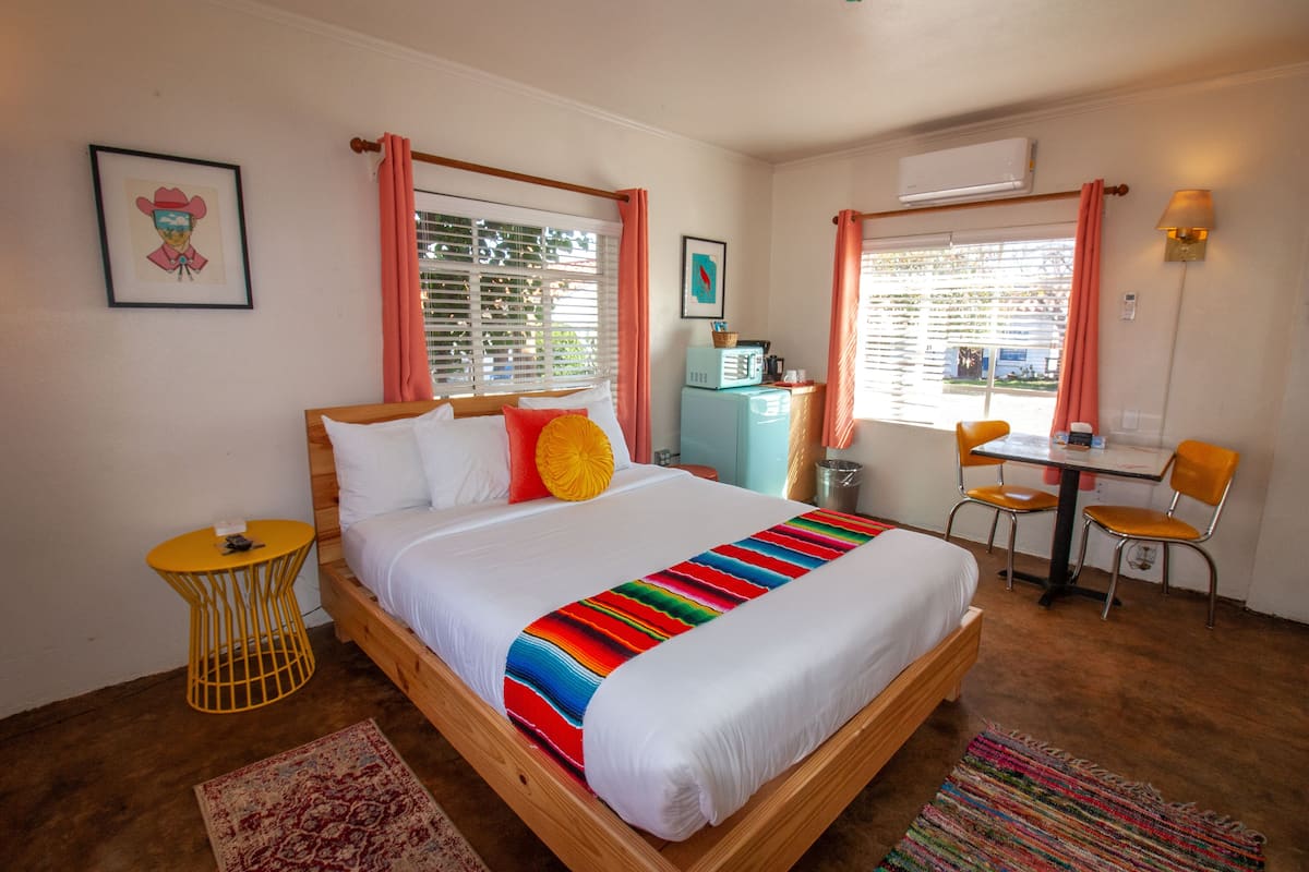 Une chambre à coucher avec un lit en bois, une petite table avec des chaises, un bureau et une fenêtre avec des rideaux.