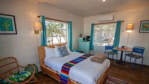 Un dormitorio con una cama de madera, dos sillas, una mesita y una ventana con cortinas.
