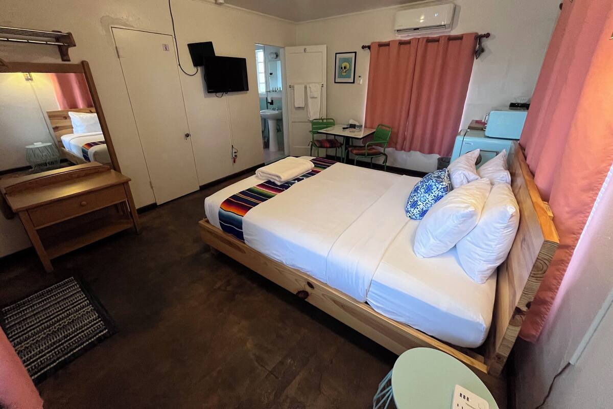 Une chambre d’hôtel équipée d’un lit, d’un bureau, d’une chaise, d’un miroir, d’une télévision et d’un appareil de climatisation.