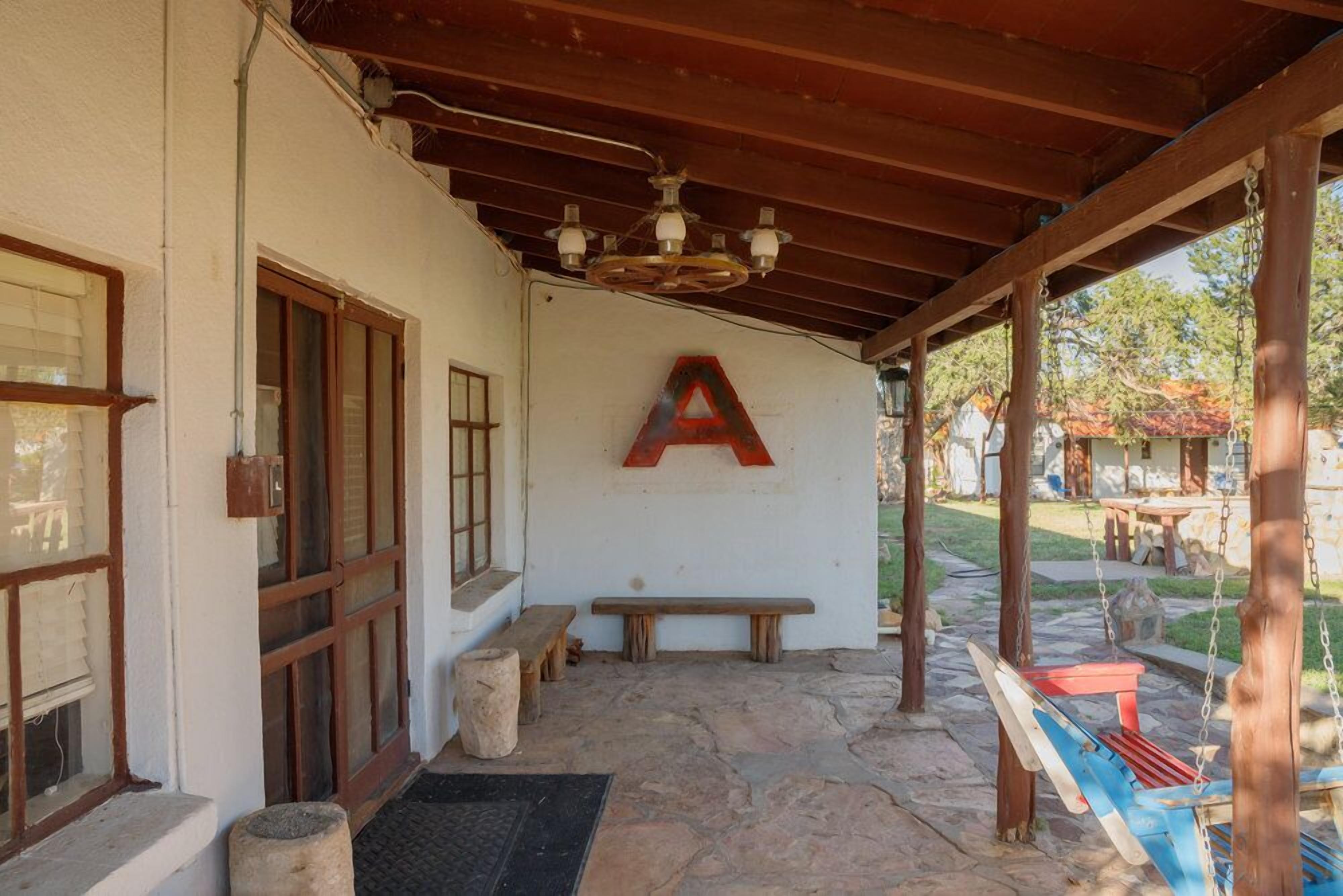 A covered patio area with a stone floor, wooden benches, a swing, and a large 'A' mounted on the wall.