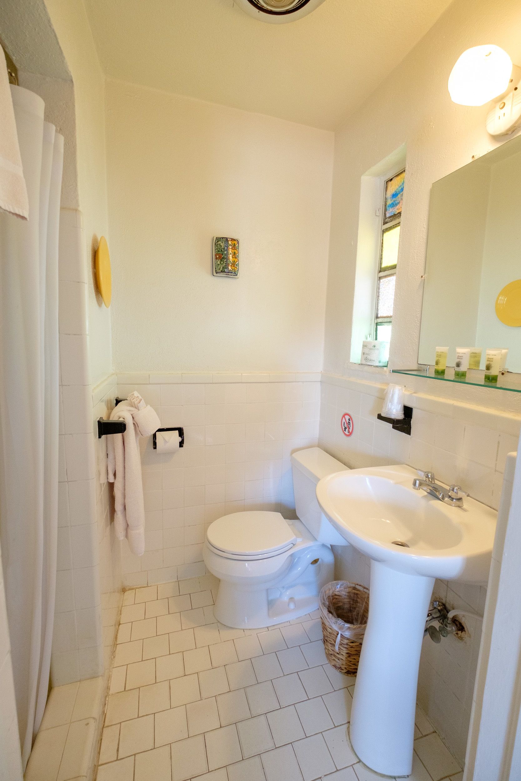 A small, clean bathroom with a toilet, sink, and shower. There is a towel rack, a small shelf with toiletries, and a decorative item on the wall.