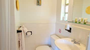 A small, clean bathroom with a toilet, sink, and shower. There is a towel rack, a small shelf with toiletries, and a decorative item on the wall.