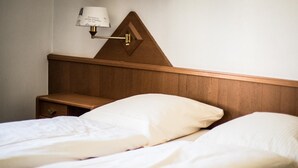 En dobbeltseng med hvide sengetæger, et træsengegærde, et natbord og en lampe fastgjort til væggen.