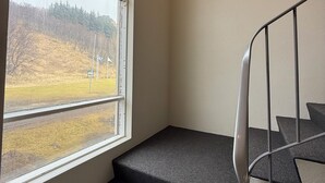 A staircase with dark carpeted steps leading to a landing, adjacent to a window with a view of a hilly landscape.