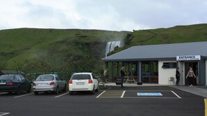 A parking area with cars, a building labeled "Entrance Restaurant & Reception," and a waterfall in the background.