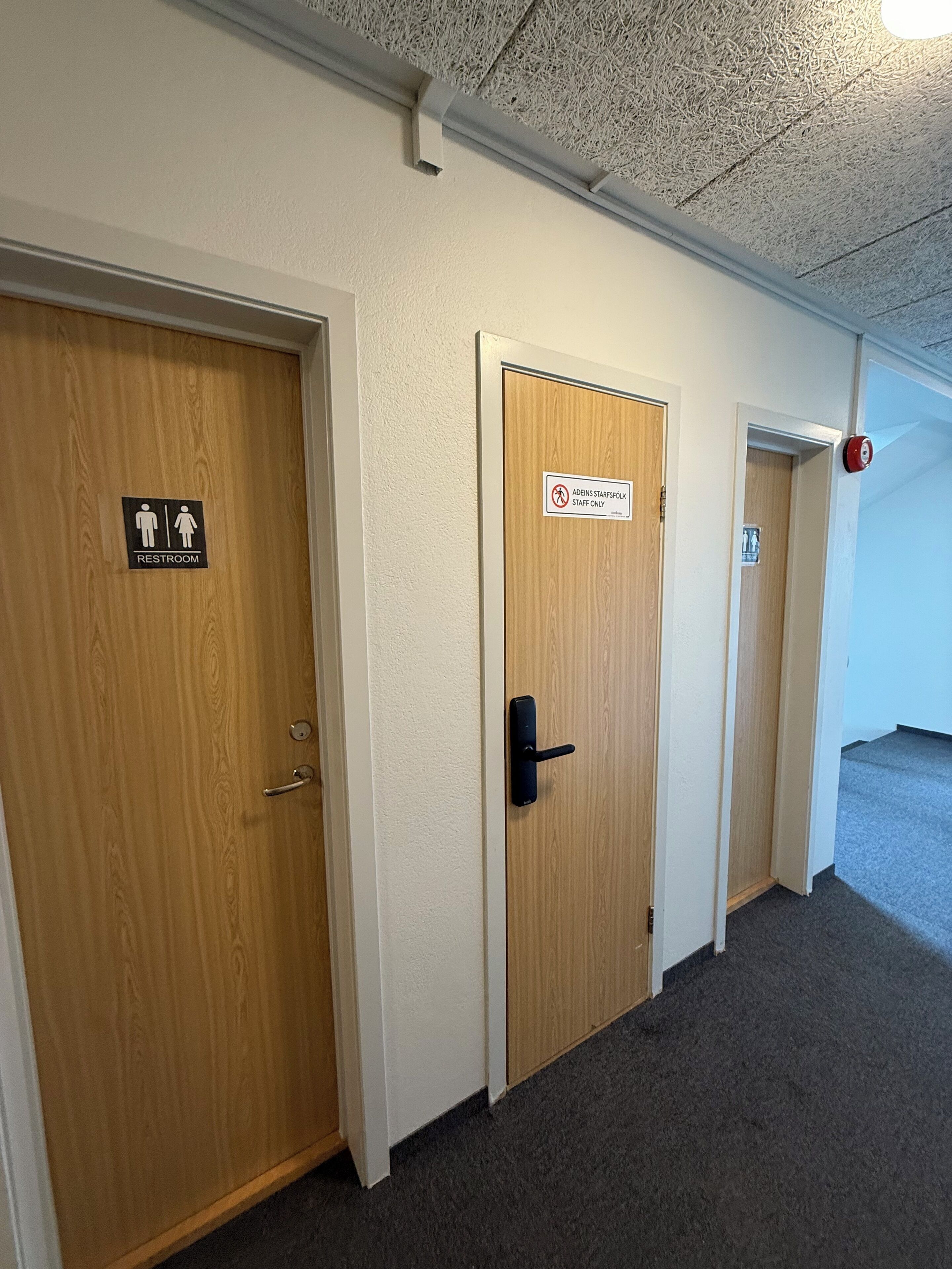 A hallway with three doors, one marked for staff use, another for restrooms, and a third door leading to a room.