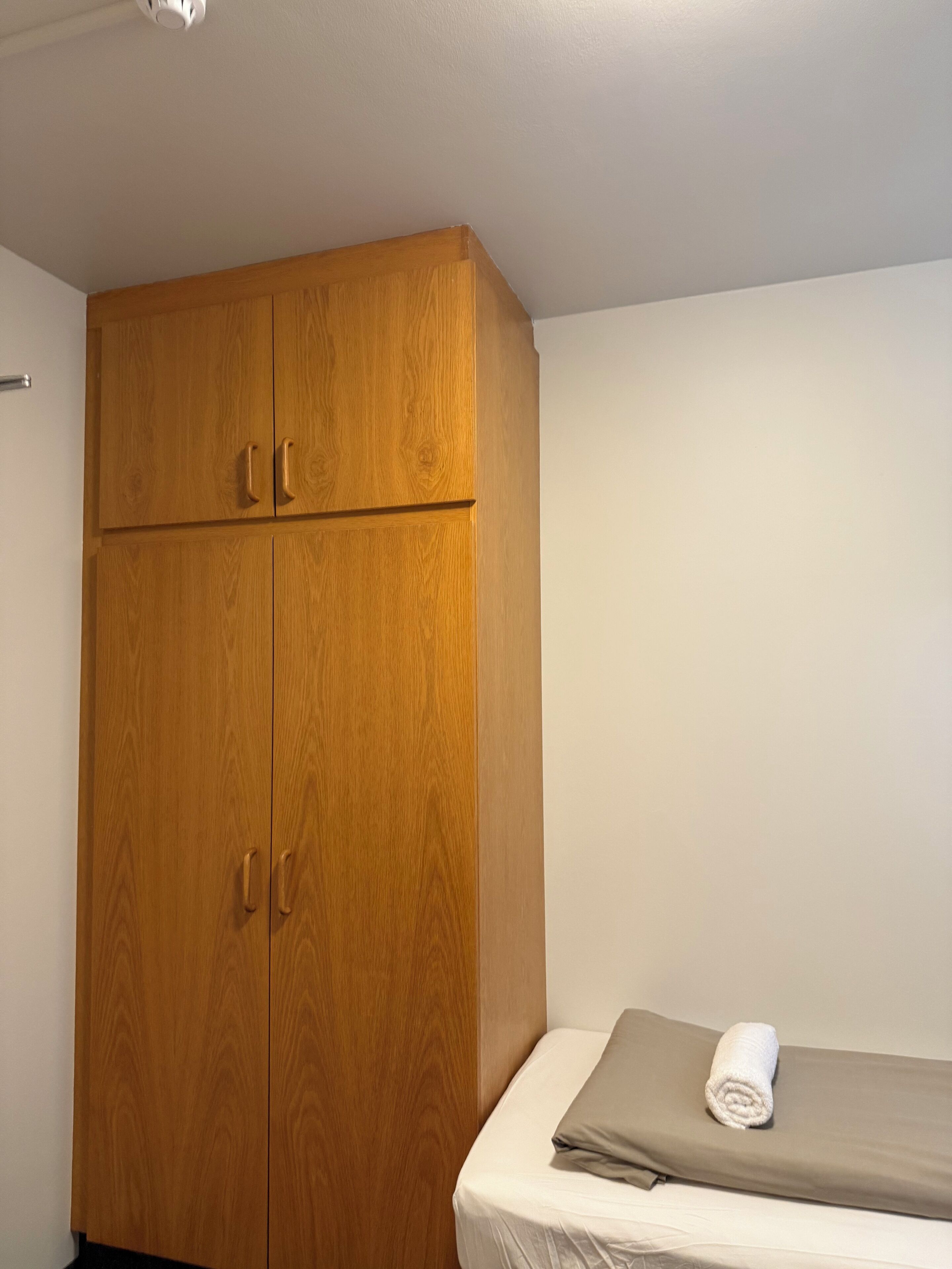Un armario de madera con dos puertas y una cama con una toalla doblada.