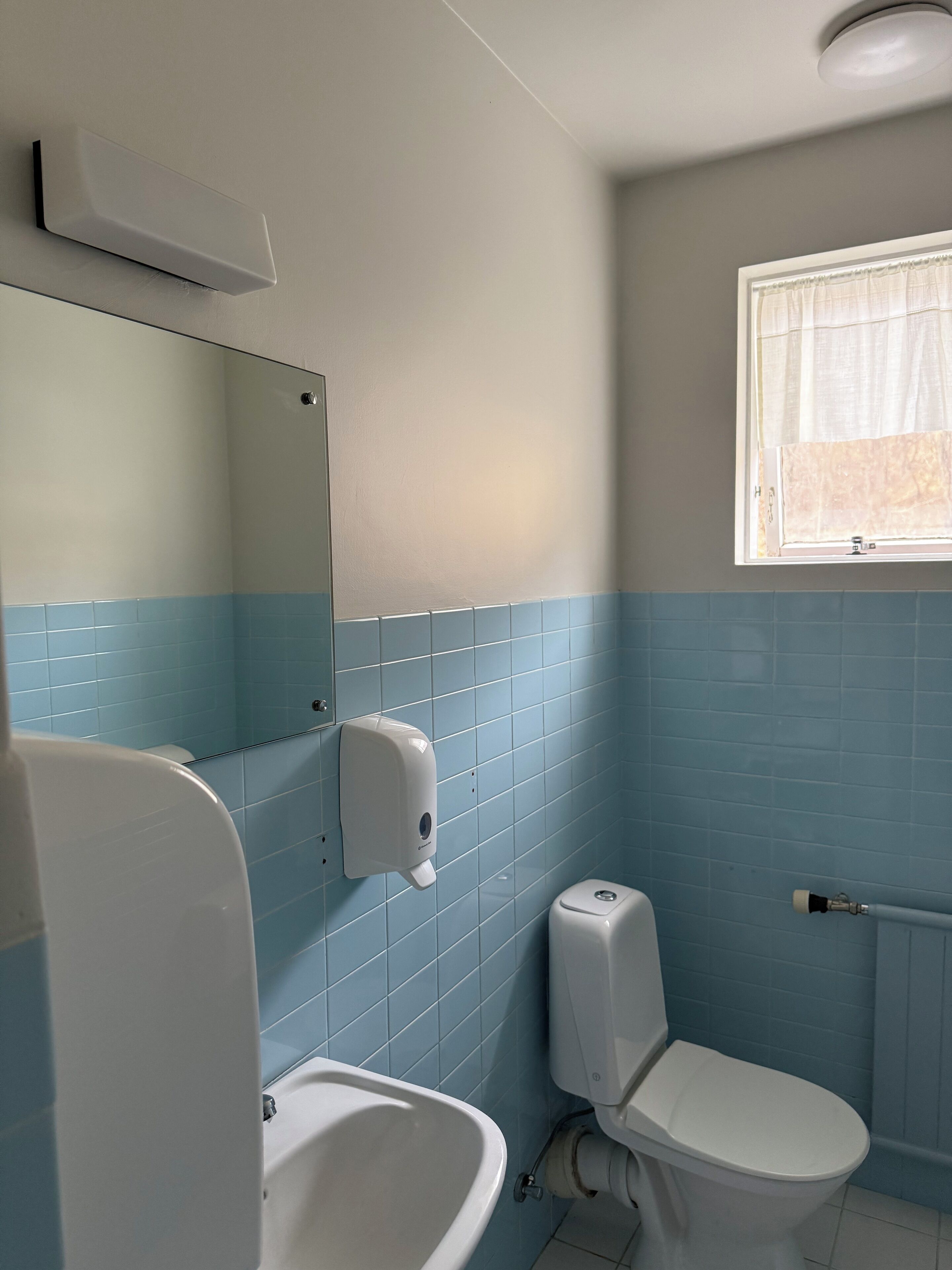A bathroom with a toilet, bidet, and a hand soap dispenser mounted on the wall.