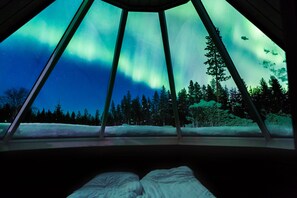 Quarto com cama e janela com vista para a aurora boreal.