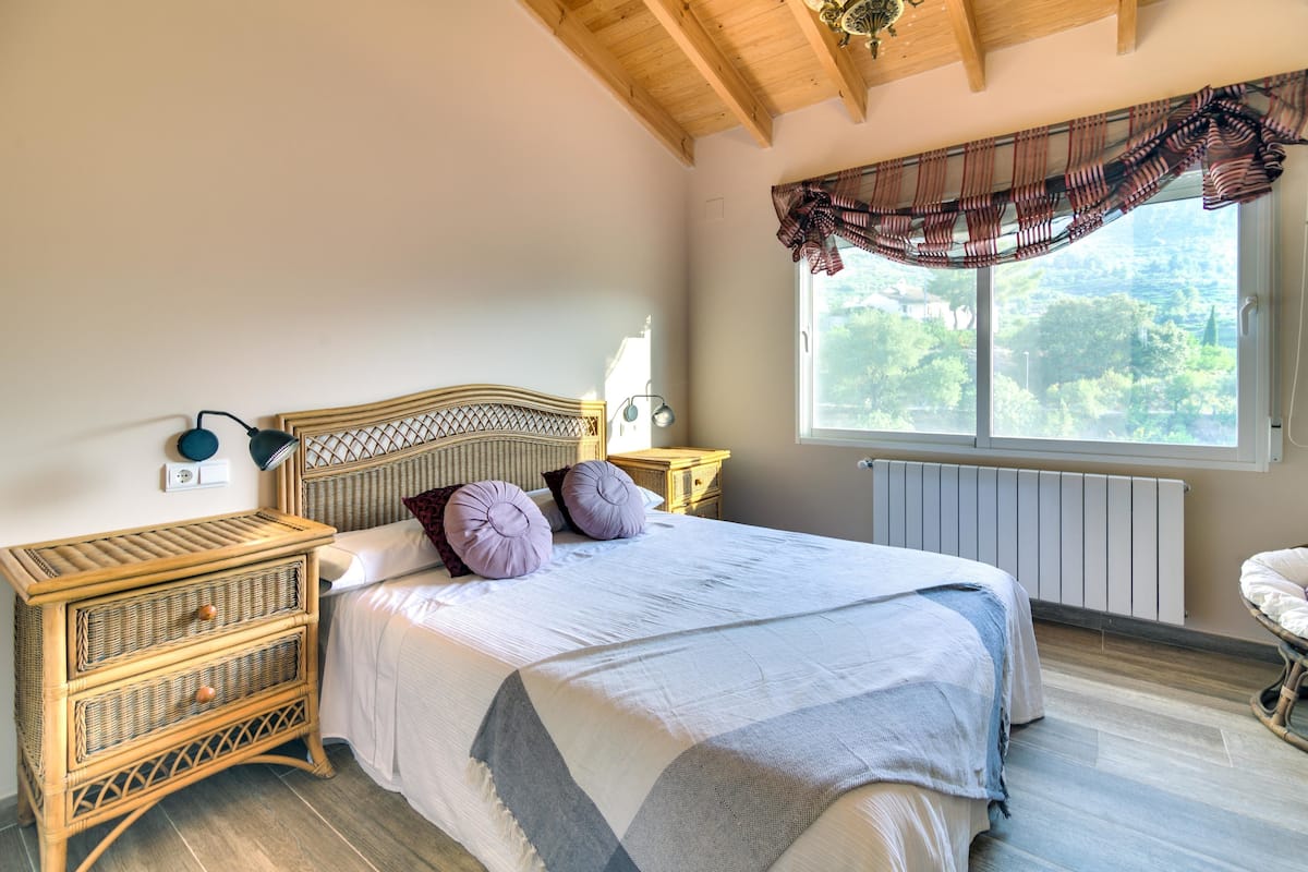 A bedroom with a bed, wooden nightstands, a window with a view, and a ceiling fan.