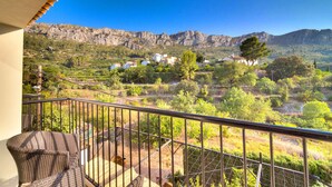 Un balcón con mobiliario de mimbre, con vistas a un paisaje montañoso salpicado de casas.