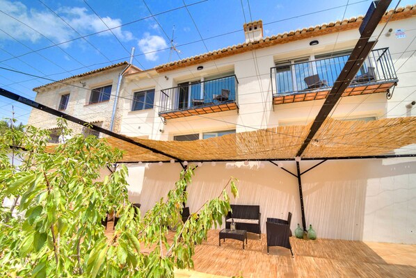 A two-story building with a balcony, a covered patio area with furniture, and a view of the sky. - El Secret de la Foradà (Vall de Gallinera)