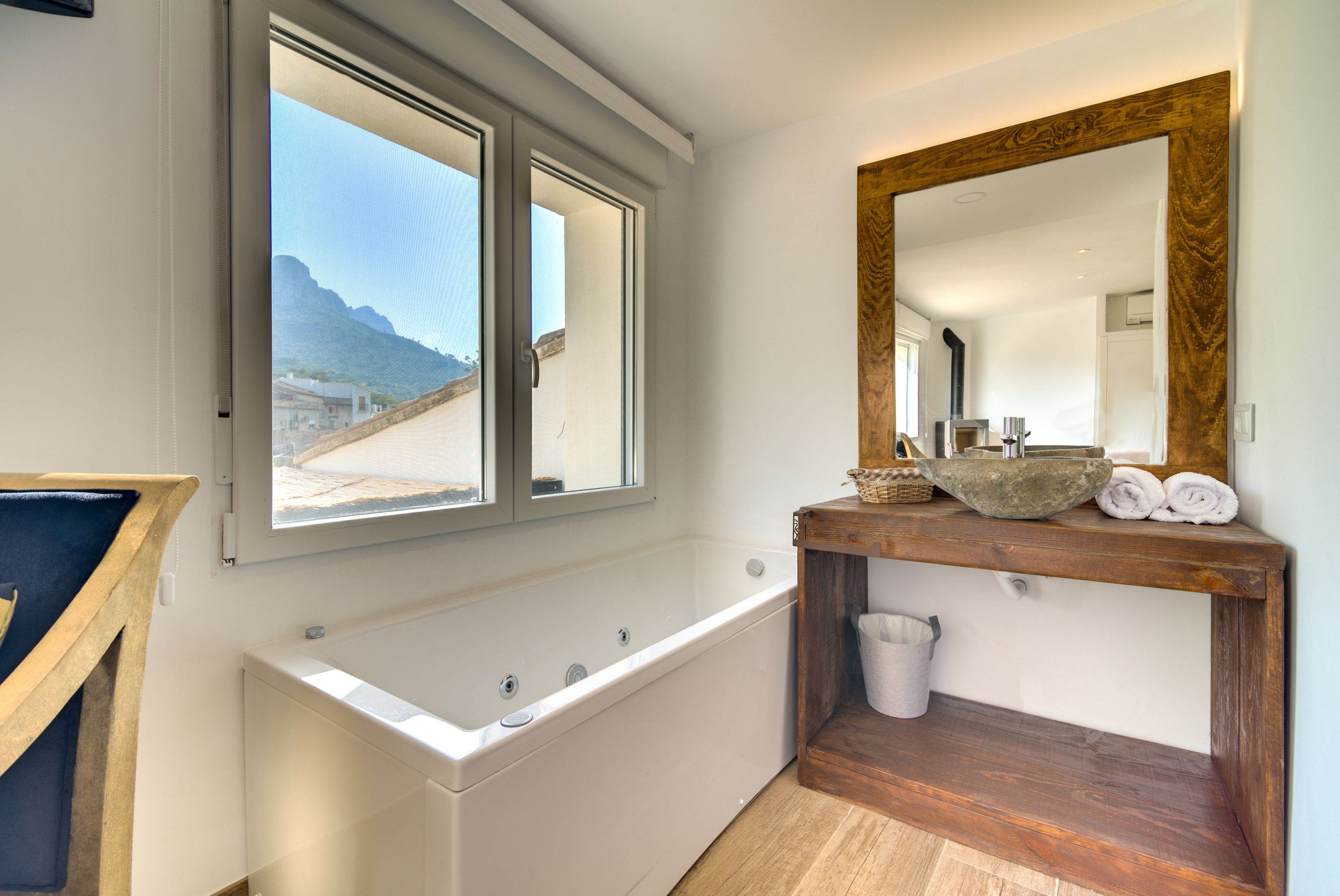 Un baño moderno con una bañera, un tocador de madera, un espejo grande y una ventana con vistas a las montañas.