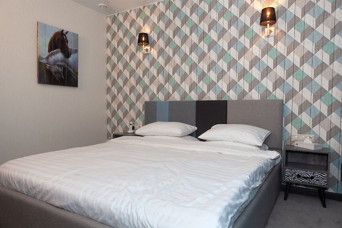 A neatly made bed with white linens, a geometric patterned wall, and two wall-mounted lamps.