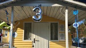 A yellow building with a white door, a number '3' sign above the door, and a small window with lace curtains. - FinnDome- Glamping (Pori)