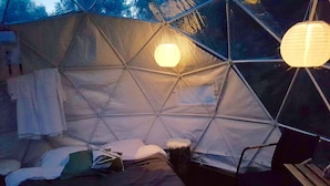 A tent with a bed, pillows, a blanket, and hanging lights. - FinnDome- Glamping (Pori)