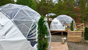 Transparent geodesic dome structures with a wooden deck in front. - FinnDome- Glamping (Pori)