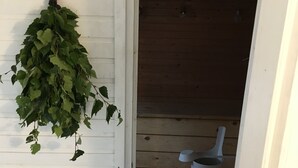 A white door with a hanging plant, a wooden wall, and a trash can inside a room. - FinnDome- Glamping (Pori)