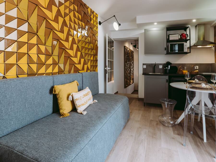 Una sala de estar moderna con un sofá gris, un papel tapiz con diseño y una zona de comedor con mesa y sillas.
