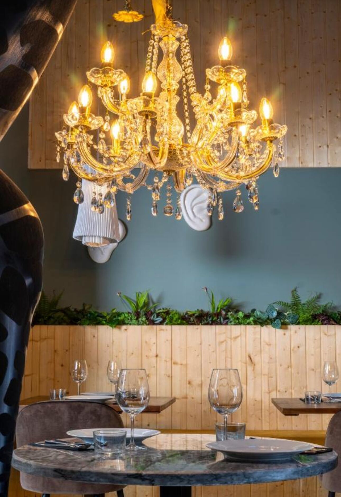 Comedor con candelabro, paneles de madera y pared vegetal.