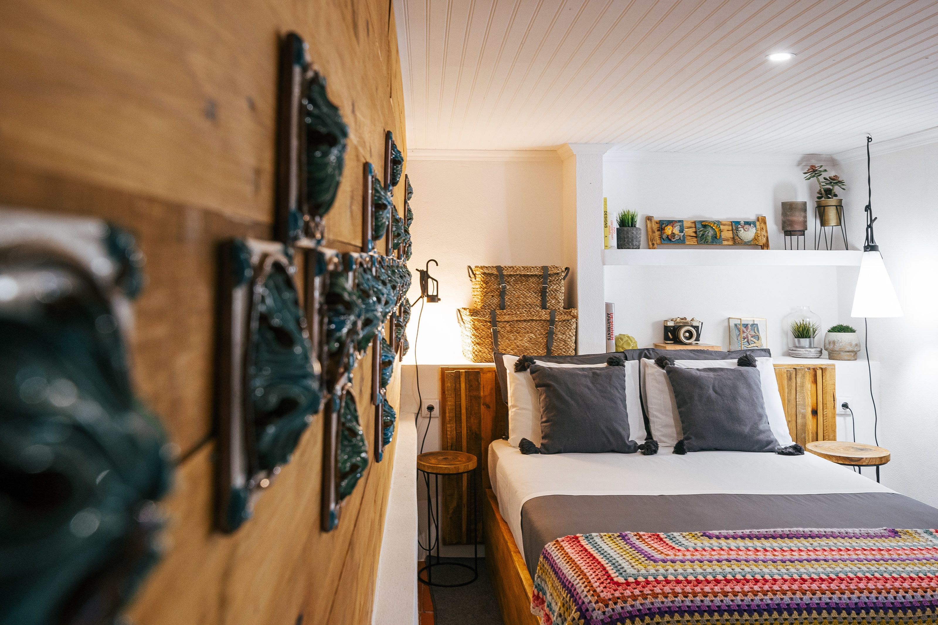A cozy bedroom with a wooden headboard, a bed with a colorful blanket, and a small wooden stool.