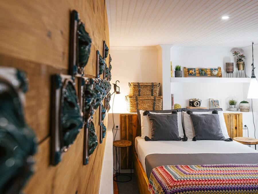A cozy bedroom with a wooden headboard, a bed with a colorful blanket, and a small wooden stool.