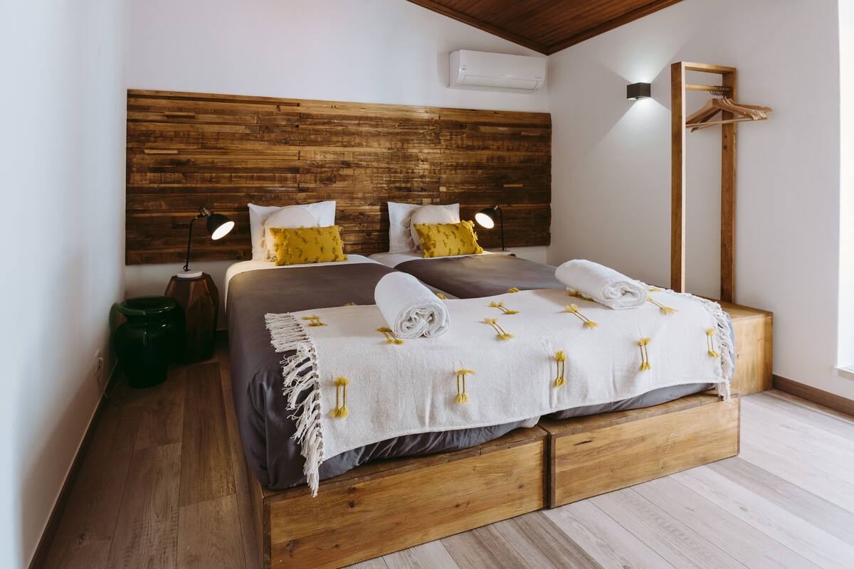 A bedroom with a wooden headboard, two bedside tables with lamps, a hanging coat rack, and a large window.
