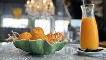 A marble countertop with a green bowl of oranges and a glass of orange juice.
