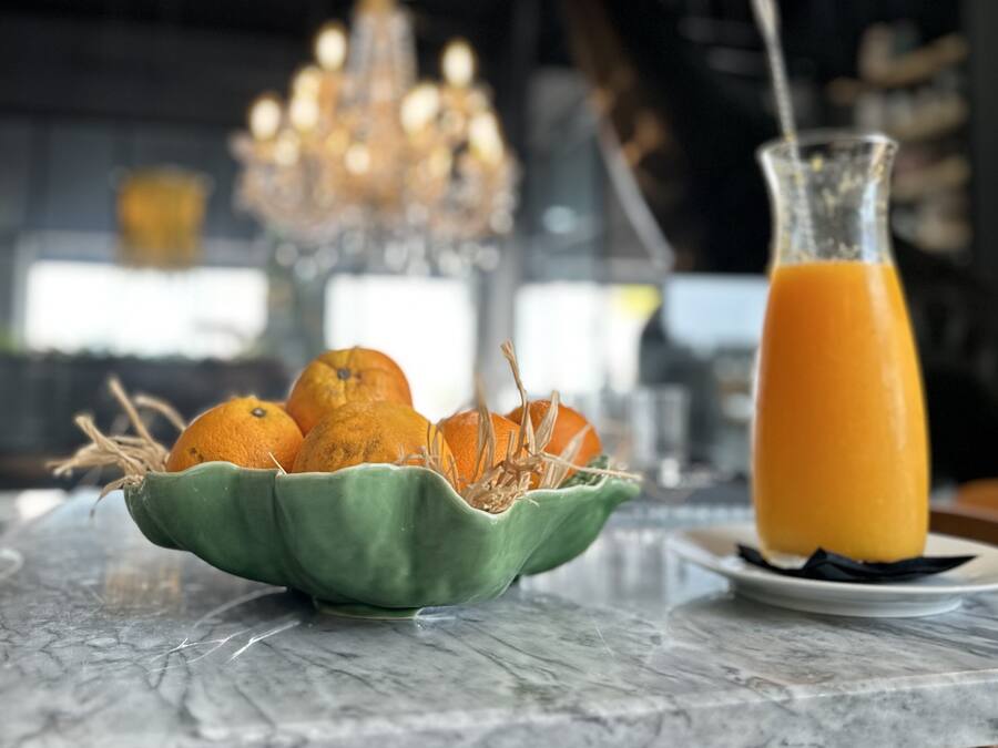 A marble countertop with a green bowl of oranges and a glass of orange juice.