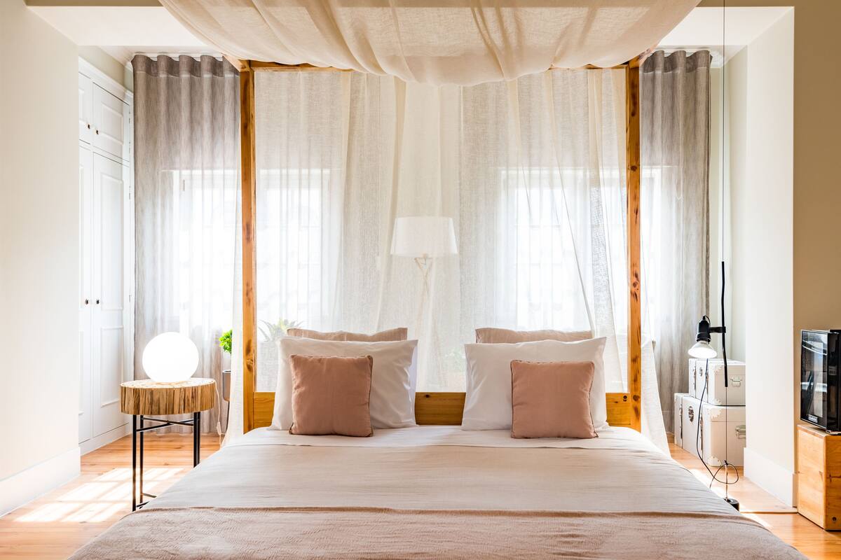 A bedroom with a large bed, a bedside table with a lamp, and curtains.