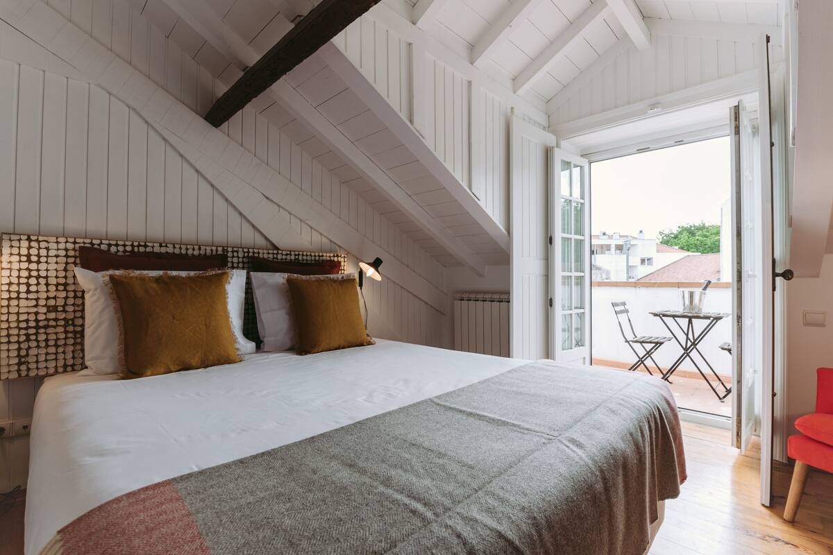 A bedroom with a large bed, a wooden ceiling, and a view of the outside.