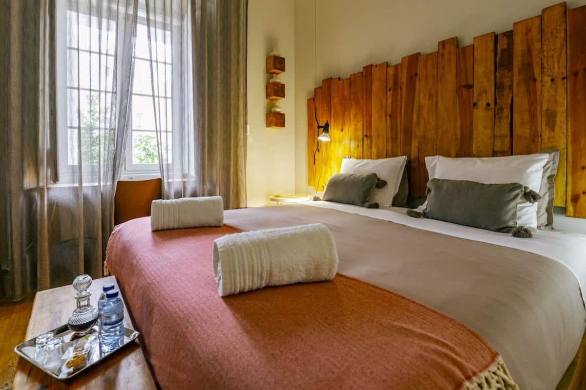 A hotel room with a large bed, wooden headboard, and a window with sheer curtains.