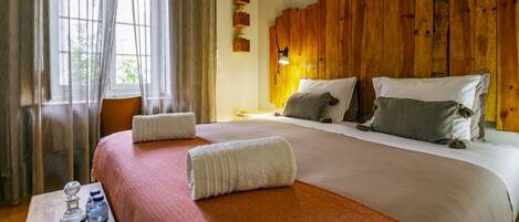 A hotel room with a large bed, wooden headboard, and a window with sheer curtains.
