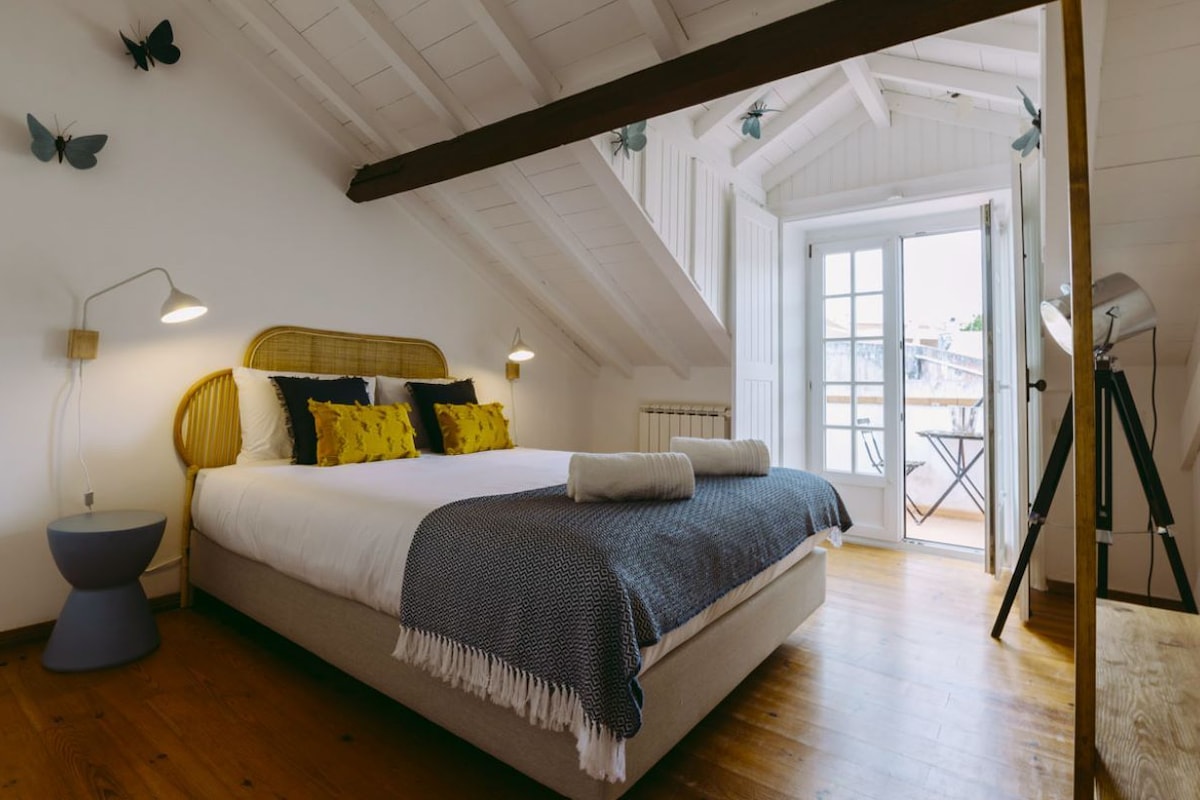 A bedroom with a bed, bedside lamps, and a view of the outdoors.