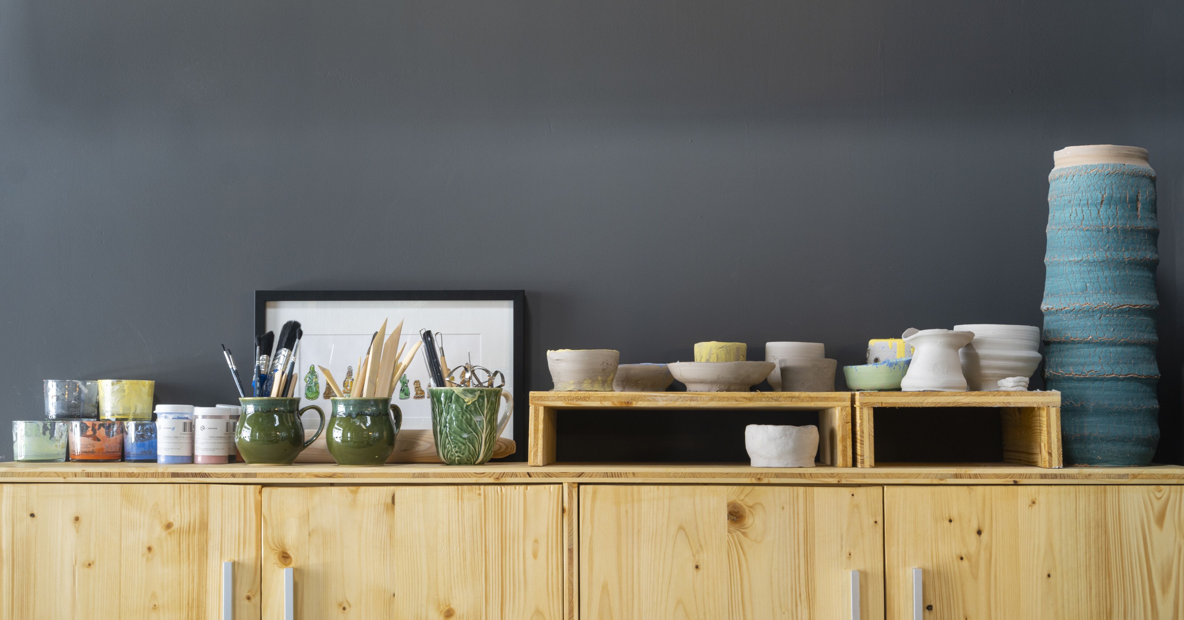 A wooden cabinet with various ceramic items and paint containers.