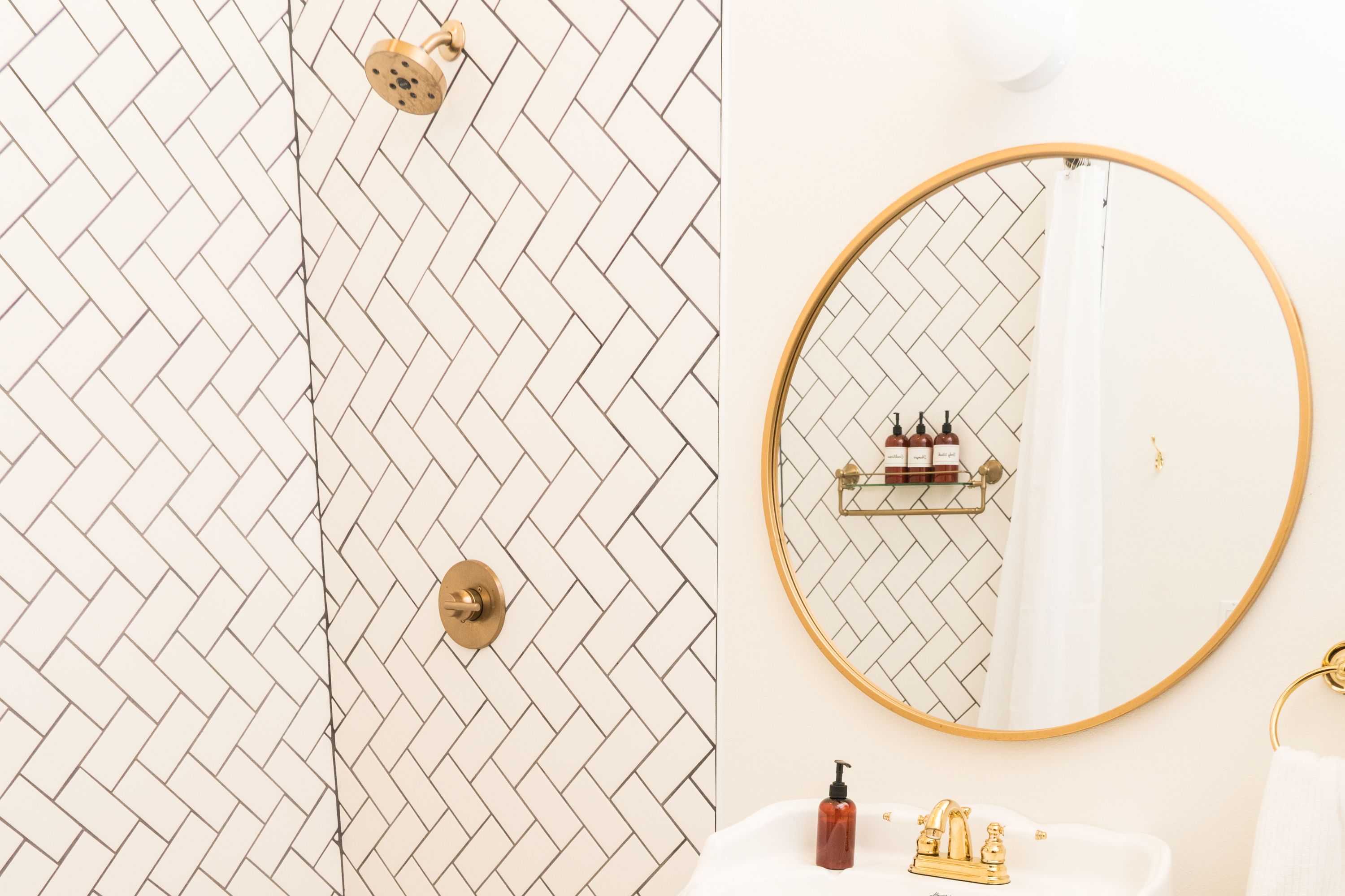 A bathroom with a herringbone tile pattern, a gold-framed mirror, and a white sink with a gold faucet.